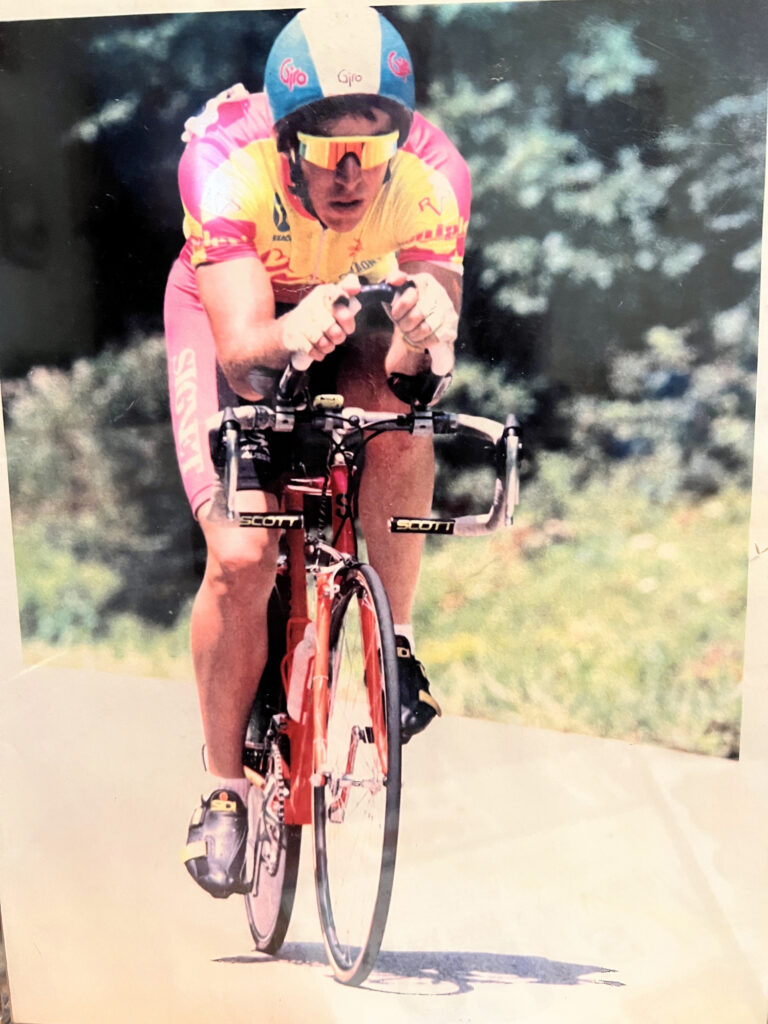 Reference photo for Intensity: a young cyclist in a yellow and pink jersey and aero helmet riding hard, taken around 1990