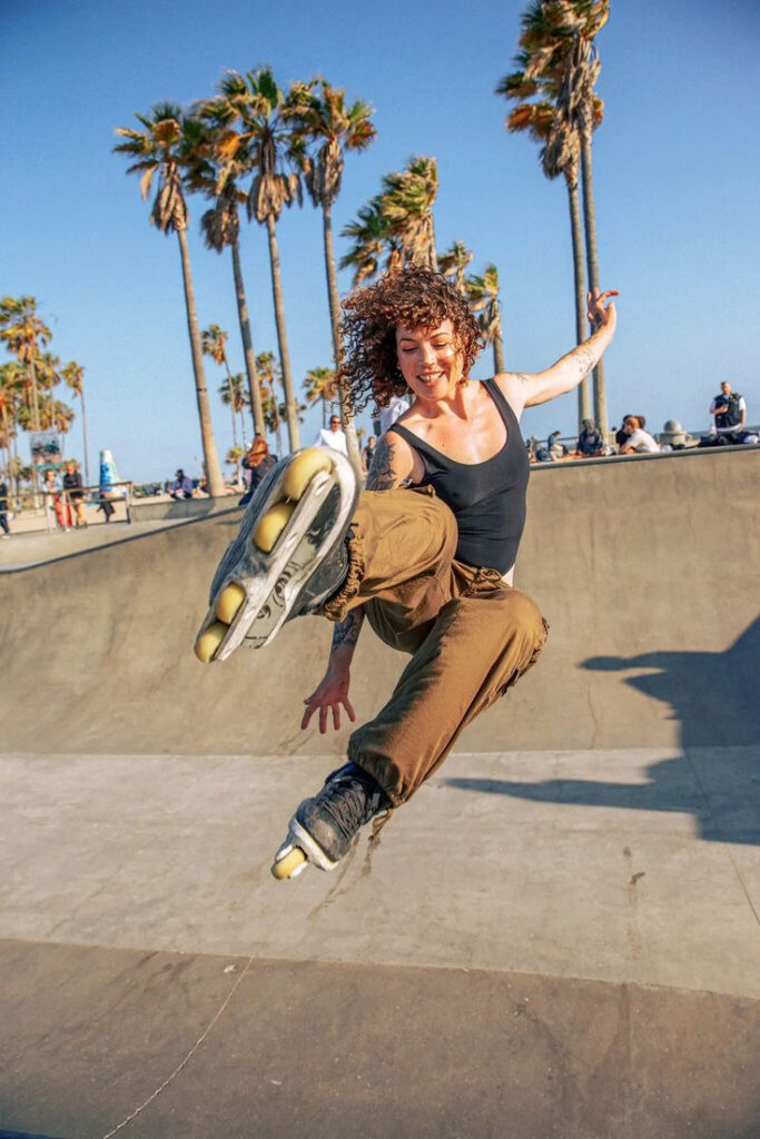 Reference photo for Joy: an inline skater in mid-air with one arm raised at a skate park lined with palm trees