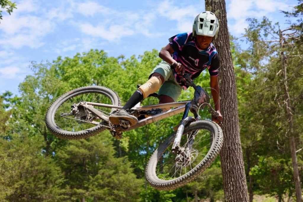 Reference photo for Send It: a mountain biker in mid-air with the bike turned sideways above the trees